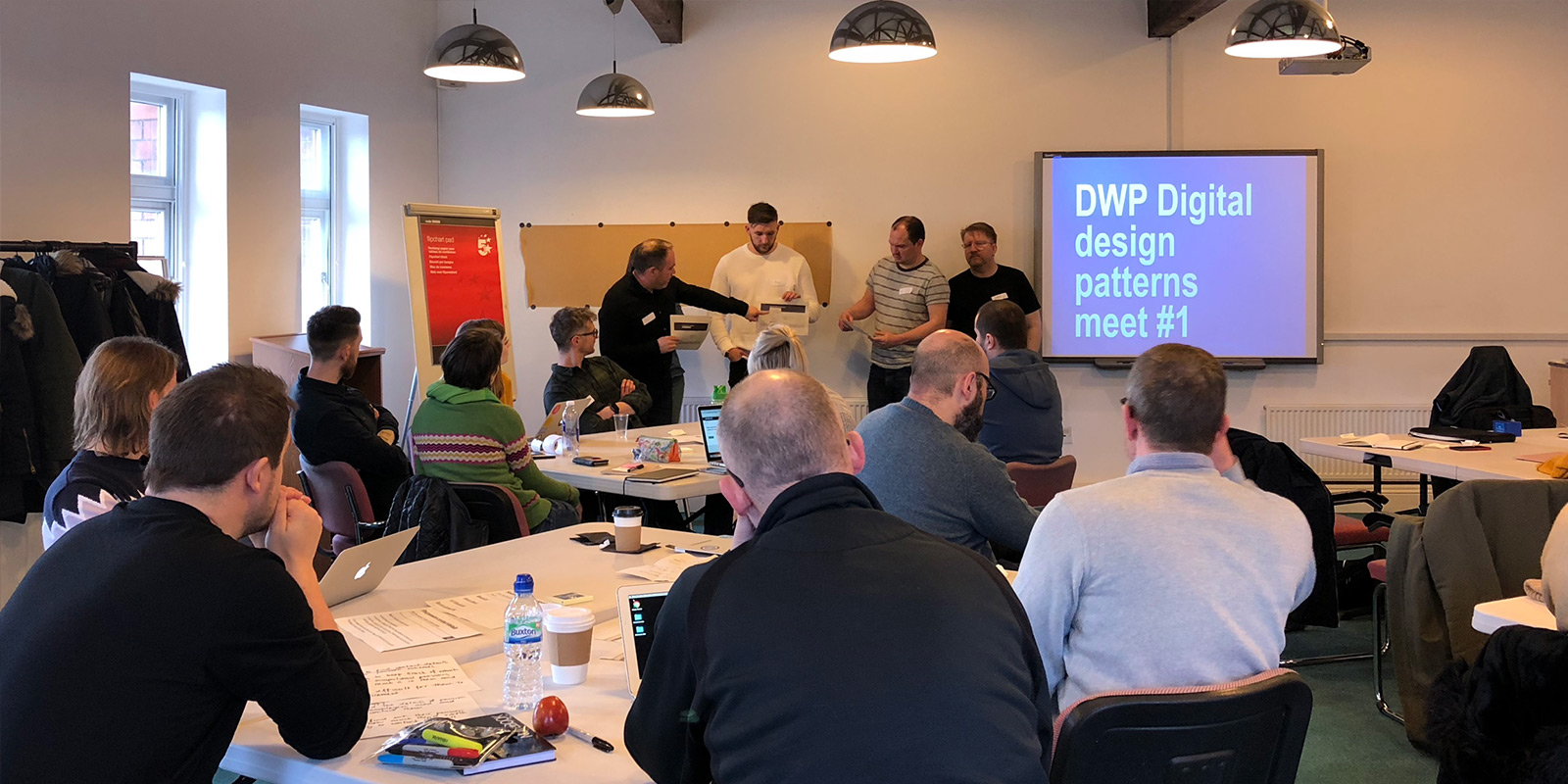 DWP Digital designers in a room listening to colleagues presenting their work